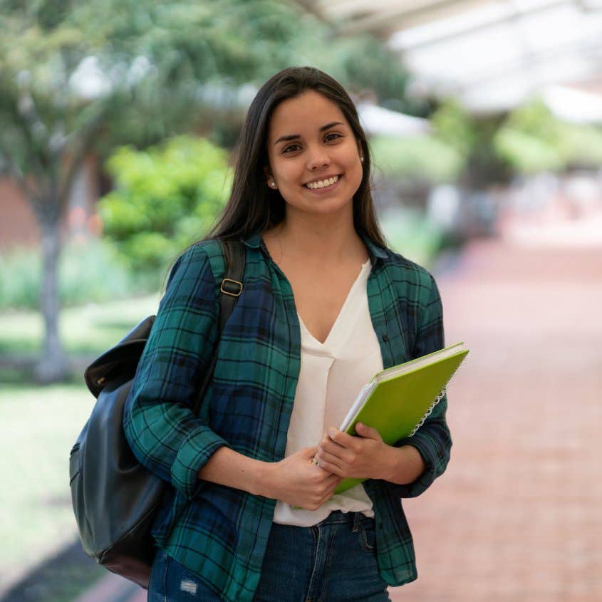 young latin american student holding her notebooks while facing camera smiling very happy at the college campus